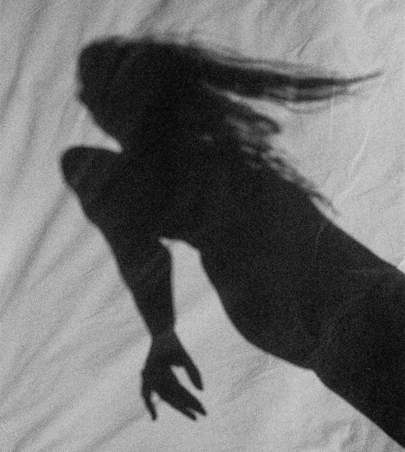 Shadow of a person's hand with long nails on a textured surface.