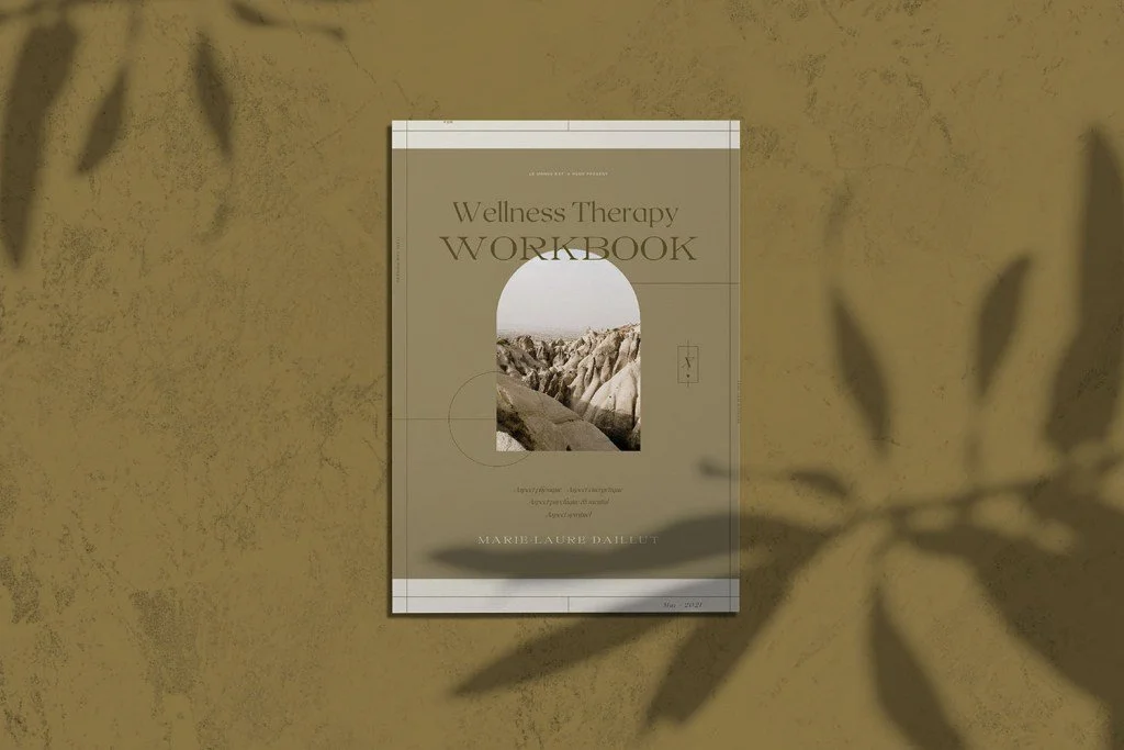 A wellness therapy workbook by Marie-laure Daillut - Le Monde est à Nous. a desert landscape photo on the cover, placed on a textured beige surface with shadows of leaves.