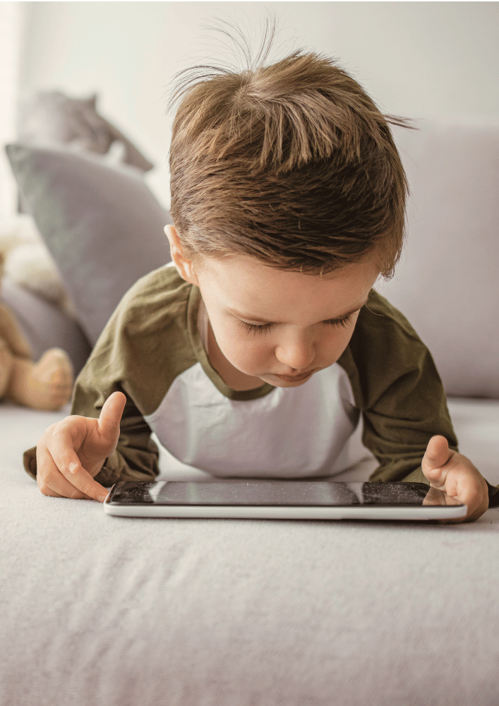 Ein Junge liegt auf dem Bauch, schaut auf ein Tablet auf einem Teppich.
