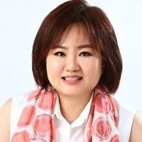 Portrait of a woman with short brown hair, smiling, wearing a white top and a pink patterned scarf.