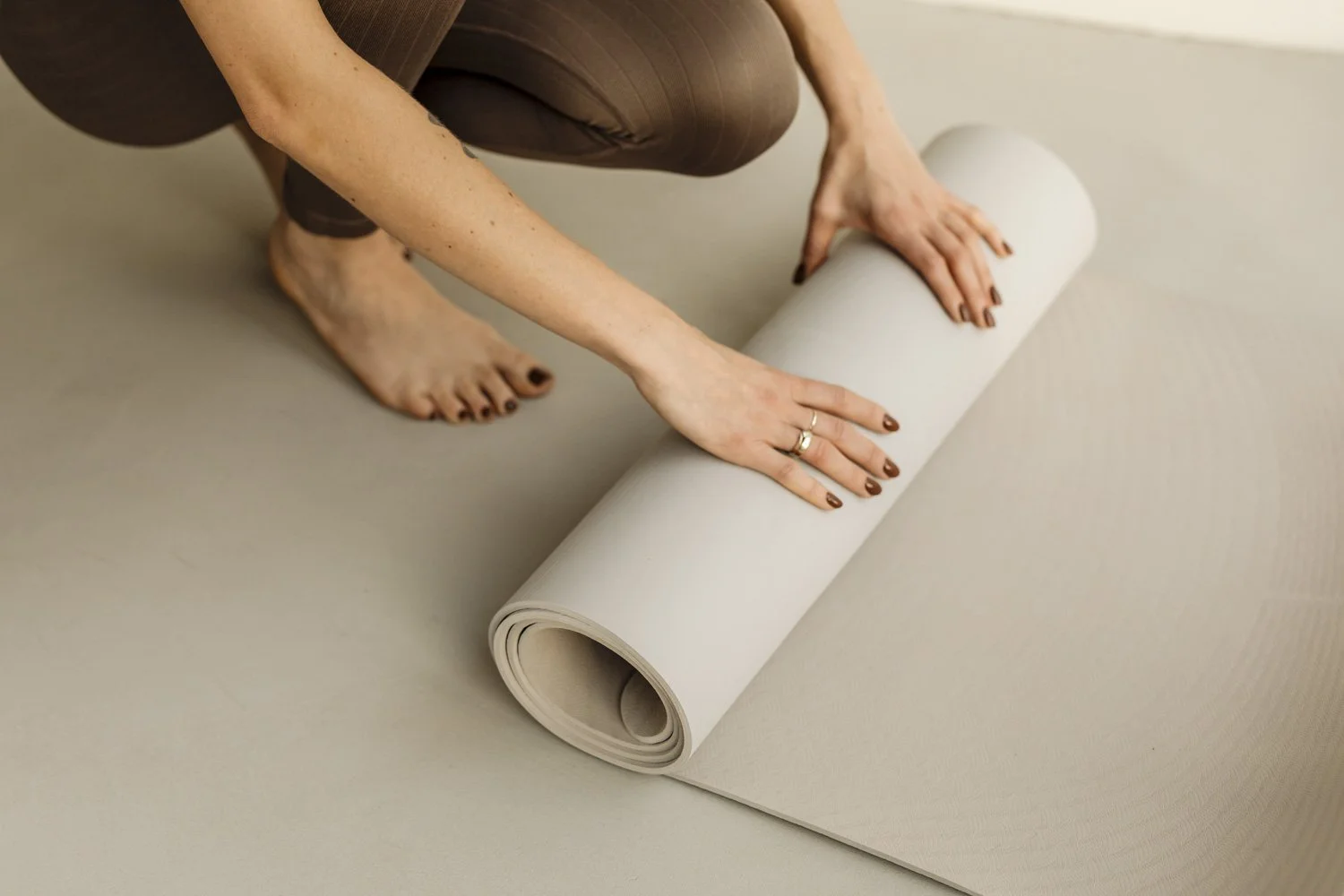 Persona arrodillada, preparando una esterilla de yoga sobre un suelo de color beige.