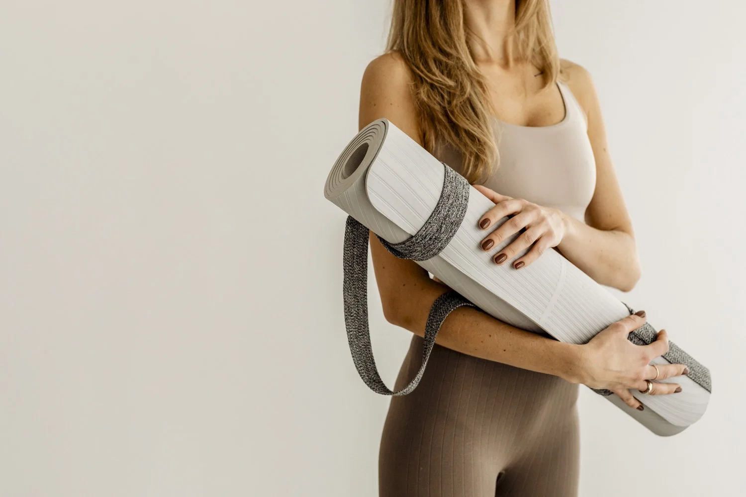 Mesa de comedor con una mesa redonda con mantel beige, rodeada de dos sillas de mimbre con estructura de metal. En la mesa hay una jarra con ramas verdes, un plato con limones, una tetera negra, una botella pequeña y un brindis con limón. Al fondo, una pared blanca decorada con un cuadro de textura abstracta, y gran ventana con puerta blanca de vidrio con diseño de líneas horizontales.