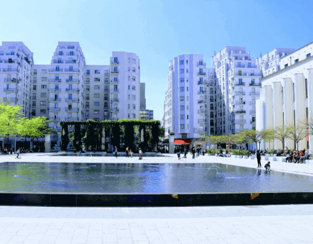 Vue d’une place urbaine moderne à Villeurbanne, avec une fontaine au centre et des bâtiments contemporains entourant un espace vert. Idéal pour découvrir comment devenir mannequin d’essayage à Villeurbanne, une ville dynamique et accueillante.