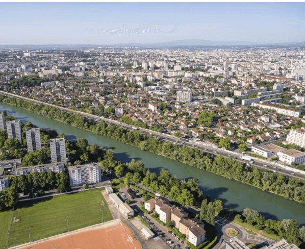 Vue aérienne panoramique de Villeurbanne, montrant la ville étendue le long d’un fleuve verdoyant. Idéal pour découvrir comment devenir mannequin d’essayage à Villeurbanne, une ville en pleine croissance avec un cadre naturel agréable.