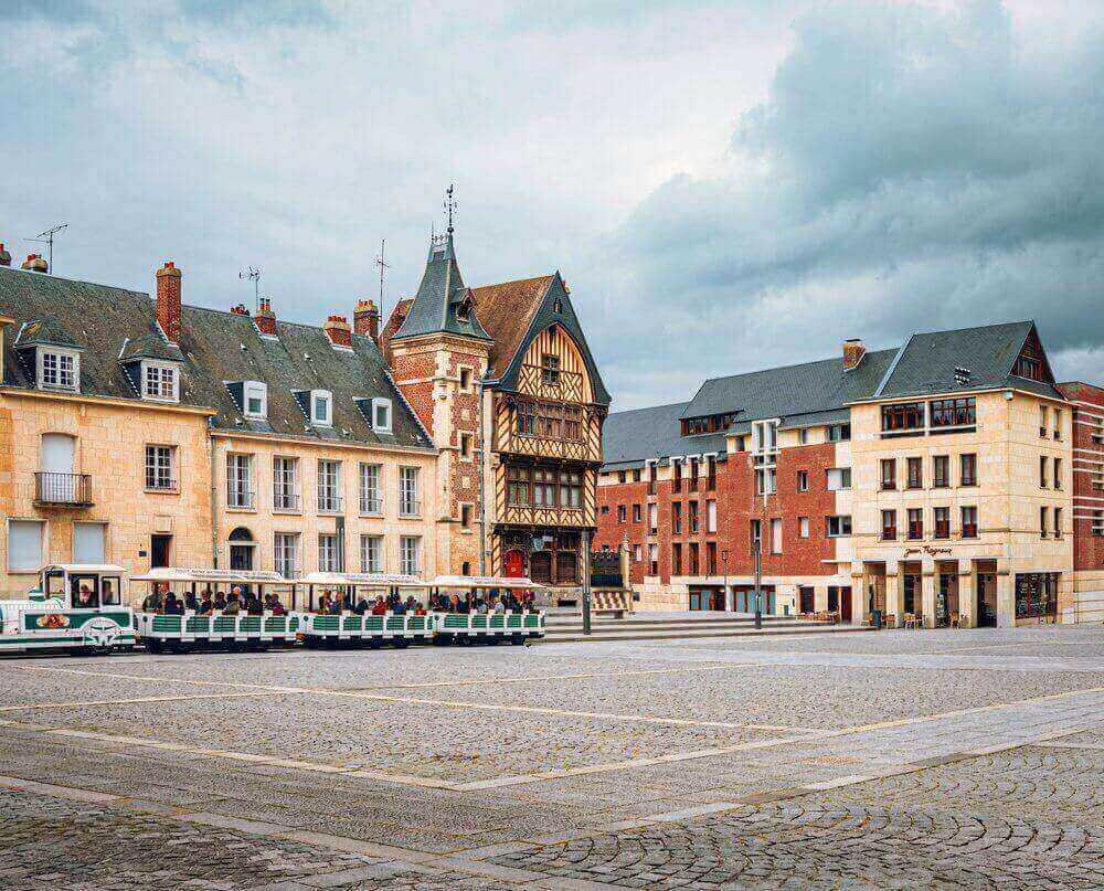 Vue panoramique d’Amiens, avec un tramway circulant dans une place bordée d’immeubles typiques. Idéal pour découvrir notre agence située au cœur de cette ville dynamique.