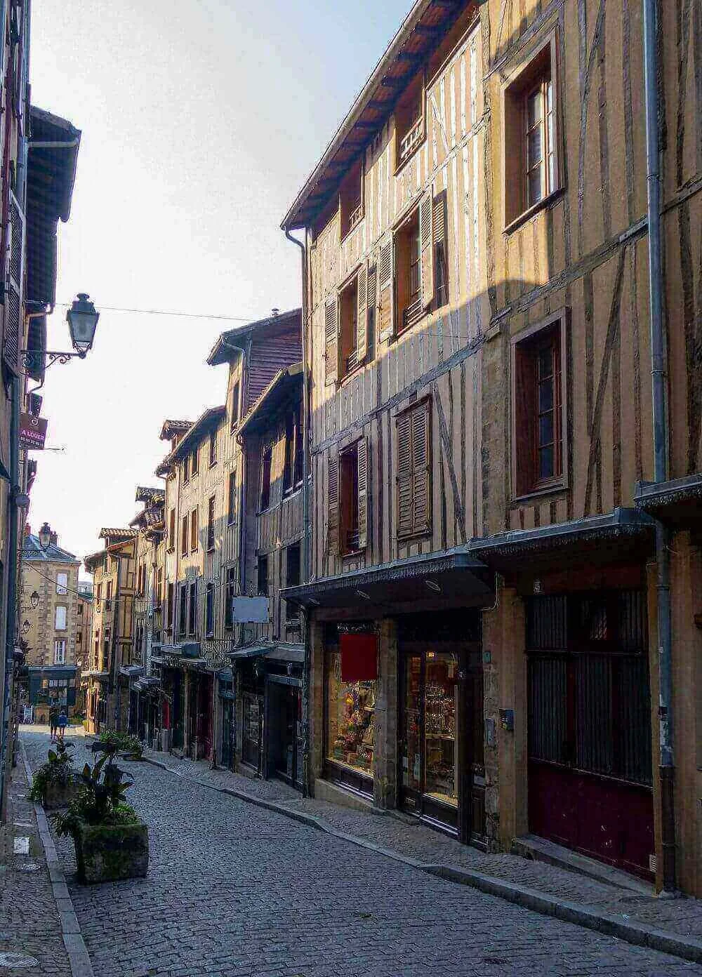 Vue d’une rue piétonne à Limoges, bordée de bâtiments en bois et pierre avec des enseignes colorées. Idéal pour découvrir notre agence et ses services d’essayage dans cette ville charmante et authentique.