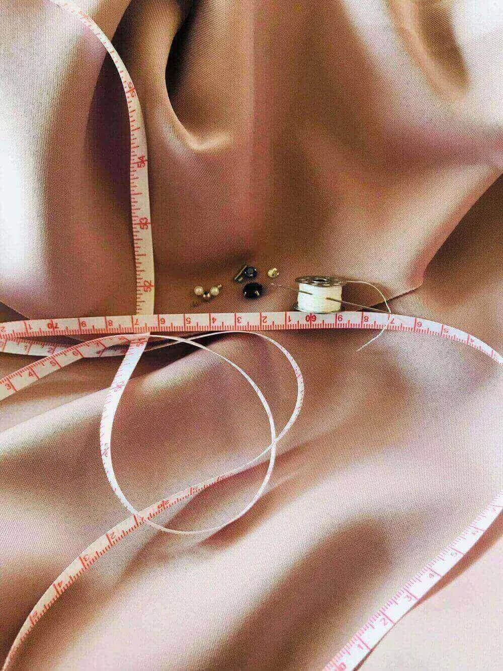 Un ruban à mesurer est utilisé pour ajuster un tissu, illustrant notre expertise dans les ajustements précis et les modifications nécessaires pour vos vêtements. Notre équipe assure un suivi rigoureux pour garantir des résultats parfaits.