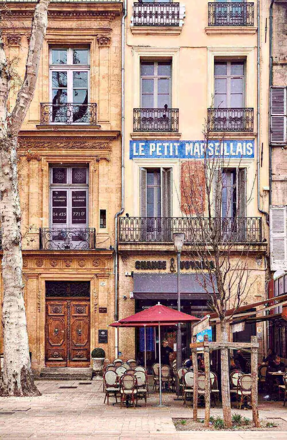Vue animée d’un café sur une place d’Aix-en-Provence, avec des tables sous un parasol rouge et des bâtiments historiques au décor provençal. Idéal pour découvrir comment devenir mannequin d’essayage.