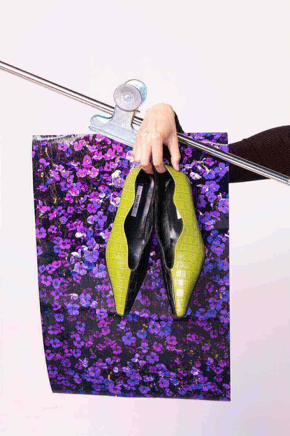 Dans cet article, The Casting Fit explique comment créer un portfolio professionnel et attractif. L’image montre une main tenant une paire de chaussures, devant un fond floral vibrant.