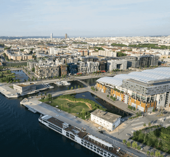 Vue aérienne panoramique du Bassin de la Confluence à Lyon, avec des bâtiments modernes et un bateau naviguant sur l’eau. Idéal pour découvrir comment devenir mannequin d’essayage à Lyon.