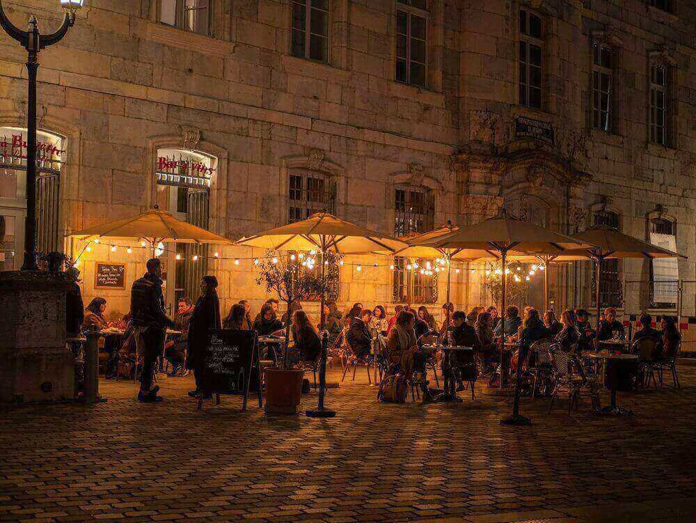 Vue d’une terrasse de café animée à Besançon, éclairée par des guirlandes lumineuses, idéale pour découvrir comment devenir mannequin d’essayage à Besançon.