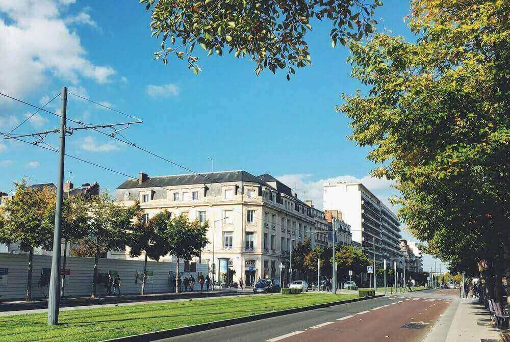 Vue d’une rue animée à Angers, bordée d’arbres et de bâtiments historiques, avec un tramway en ligne. Idéal pour découvrir comment devenir mannequin d’essayage à Angers, une ville où l’architecture se marie avec la modernité des transports publics.