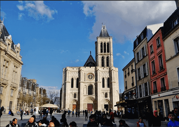 Vue d’une place animée à Saint-Denis, avec la Basilique Saint-Denis en arrière-plan et des bâtiments colorés. Idéal pour découvrir comment devenir mannequin d’essayage à Saint-Denis, une ville dynamique et accueillante.