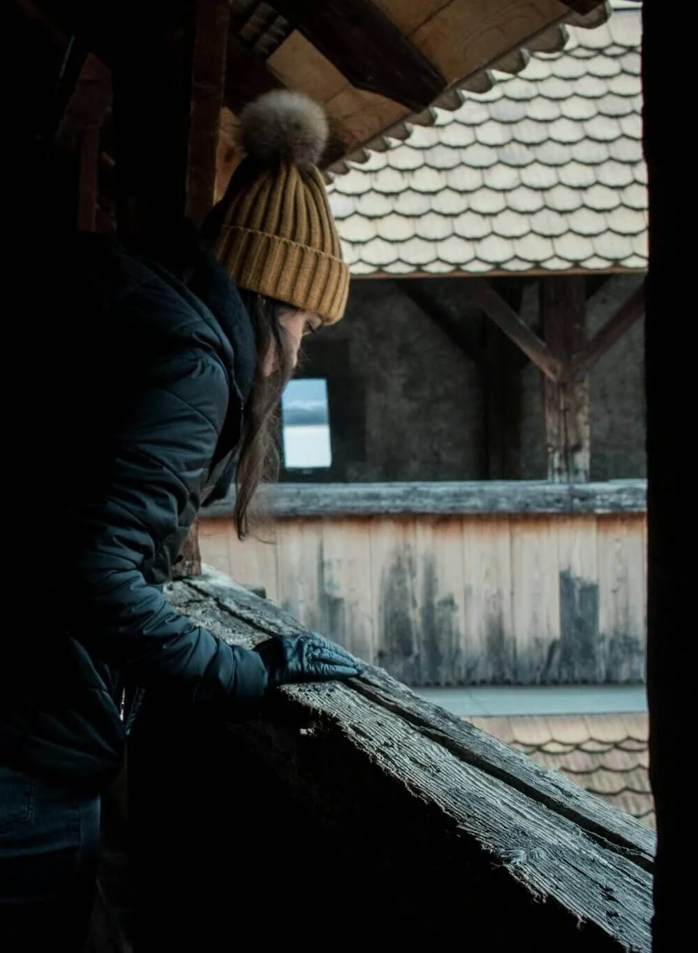 Vue d’une femme portant un bonnet et des gants, appuyée sur une balustrade en bois, contemplant une vue urbaine à Montreuil. Idéal pour découvrir comment devenir mannequin d’essayage à Montreuil, où l’architecture et la nature se rencontrent.