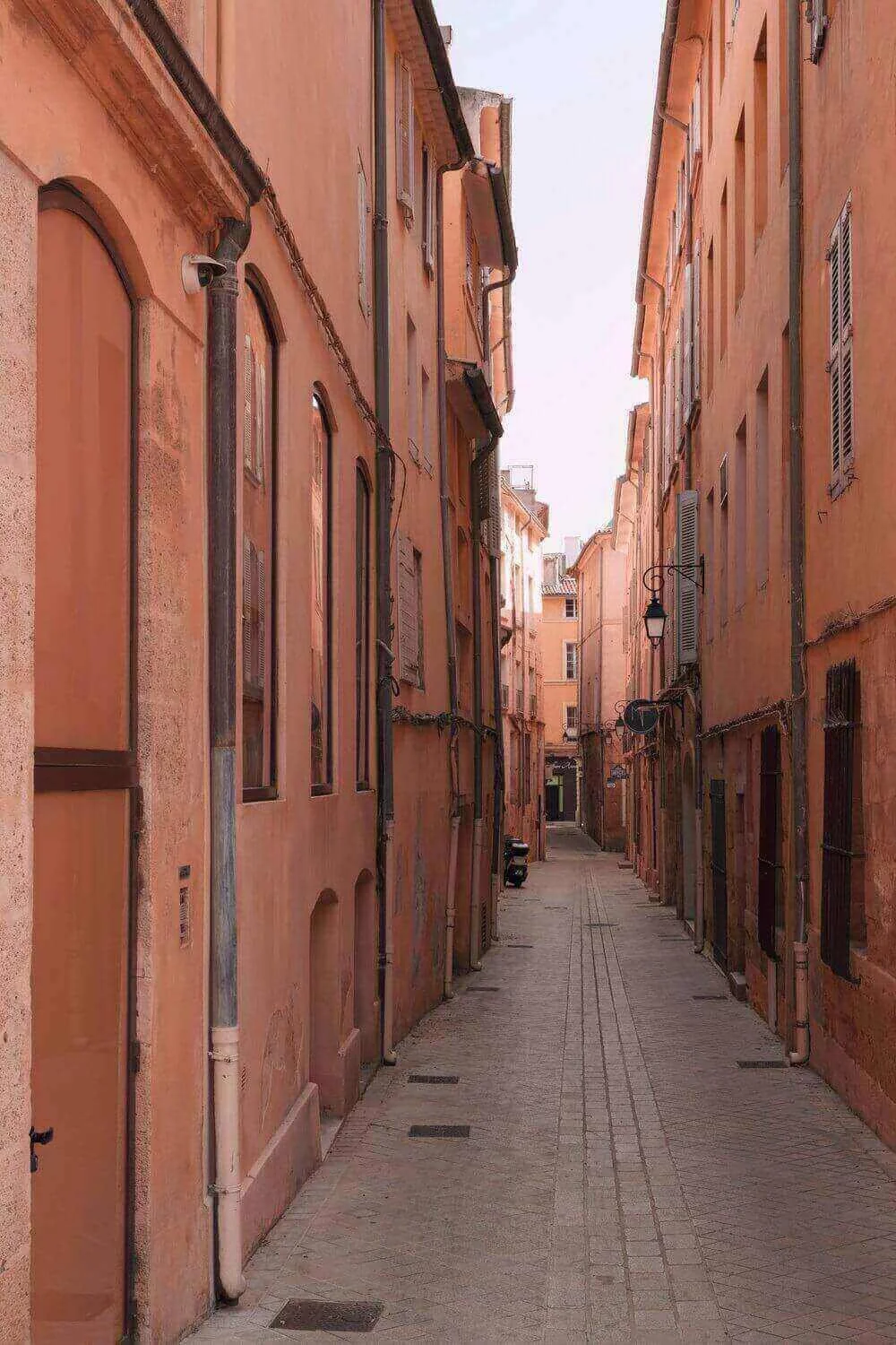 Vue d’une rue étroite et pittoresque à Aix-en-Provence, bordée de bâtiments en rose pastel. Idéal pour découvrir notre agence et ses services d’essayage dans cette ville charmante et authentique.