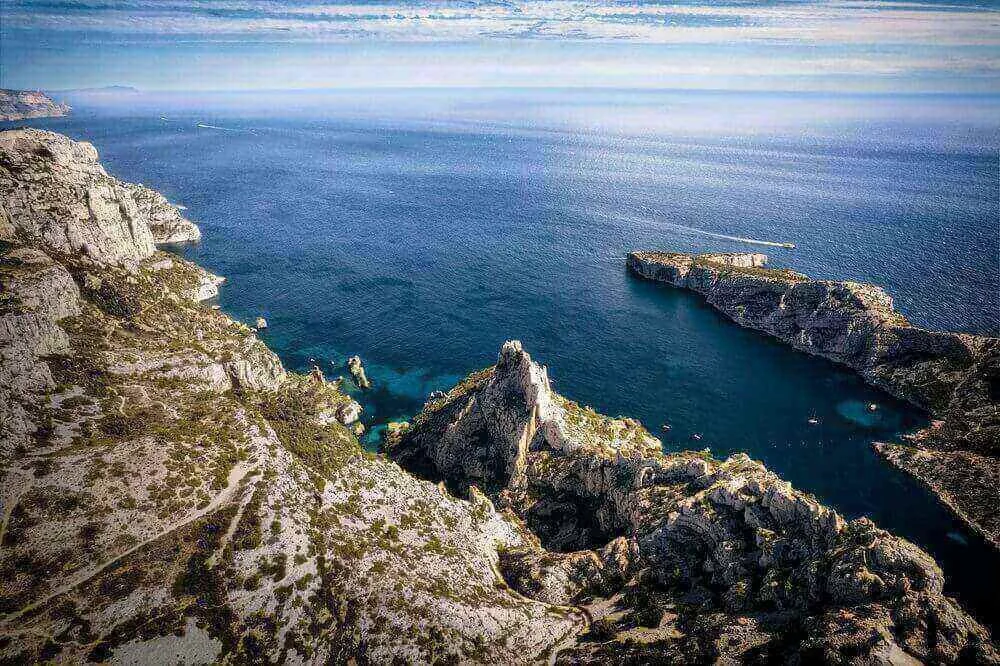 Vue aérienne panoramique des calanques de Marseille, avec des formations rocheuses spectaculaires et des eaux cristallines. Idéal pour découvrir comment devenir mannequin d’essayage à Marseille, une ville où la nature se marie avec son patrimoine.