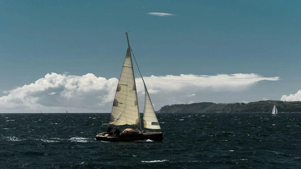 Vue d’un bateau à voile naviguant sur les eaux agitées de Brest, avec un ciel clair et des nuages en arrière-plan. Idéal pour découvrir comment devenir mannequin d’essayage à Brest, une ville côtière animée par la mer et l’aventure nautique.