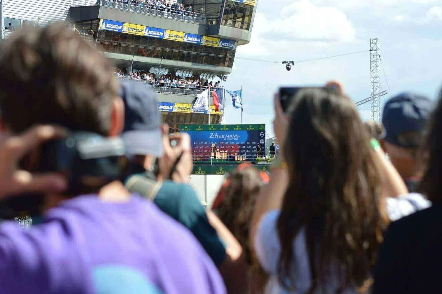 Vue dynamique des spectateurs captivant l’excitation de la course 24 Heures du Mans, avec des drapeaux et des panneaux publicitaires. Idéal pour découvrir comment devenir mannequin d’essayage au Mans.