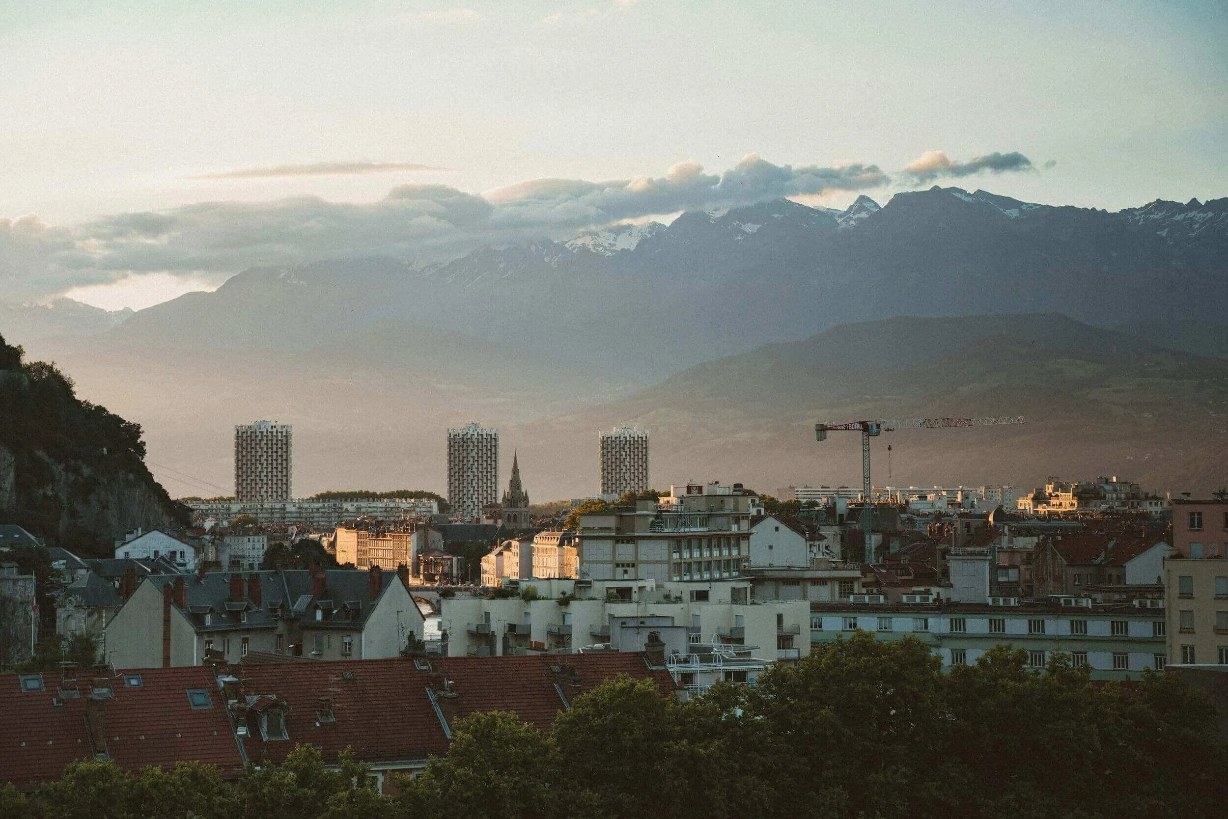 Vue panoramique de Grenoble, avec les montagnes enneigées au fond et une ville moderne en avant-plan. Idéal pour découvrir notre agence et ses services d’essayage dans cette ville dynamique, entourée de paysages alpins magnifiques.