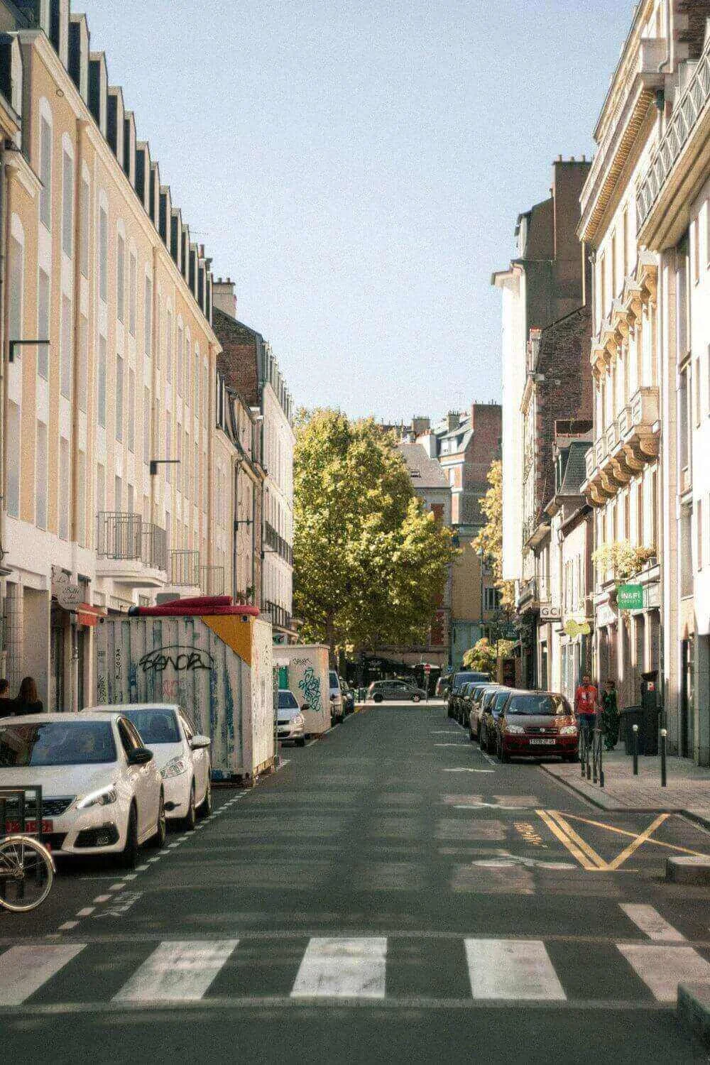 Vue d’une rue animée à Rennes, bordée de bâtiments et d’arbres, avec des voitures et des piétons. Idéal pour découvrir comment devenir mannequin d’essayage à Rennes, une ville où le charme historique se marie avec la vie quotidienne moderne.