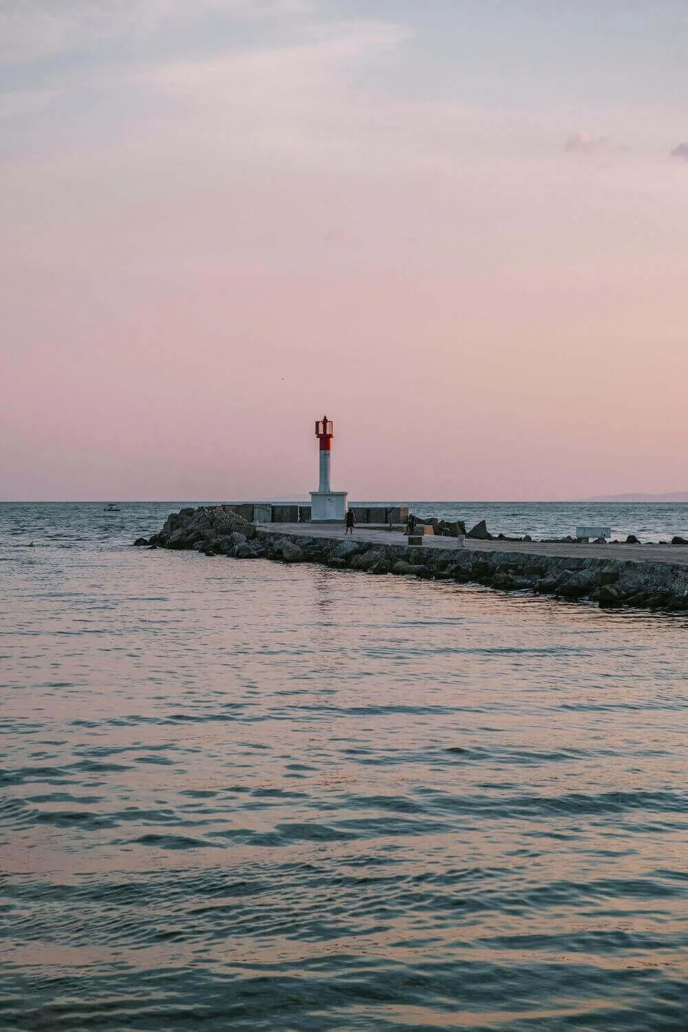 Vue paisible du Havre, avec un phare au loin et un ponton en avant-plan, reflétant le coucher de soleil. Idéal pour découvrir comment devenir mannequin d’essayage à Le Havre, une ville portuaire dynamique et accueillante.