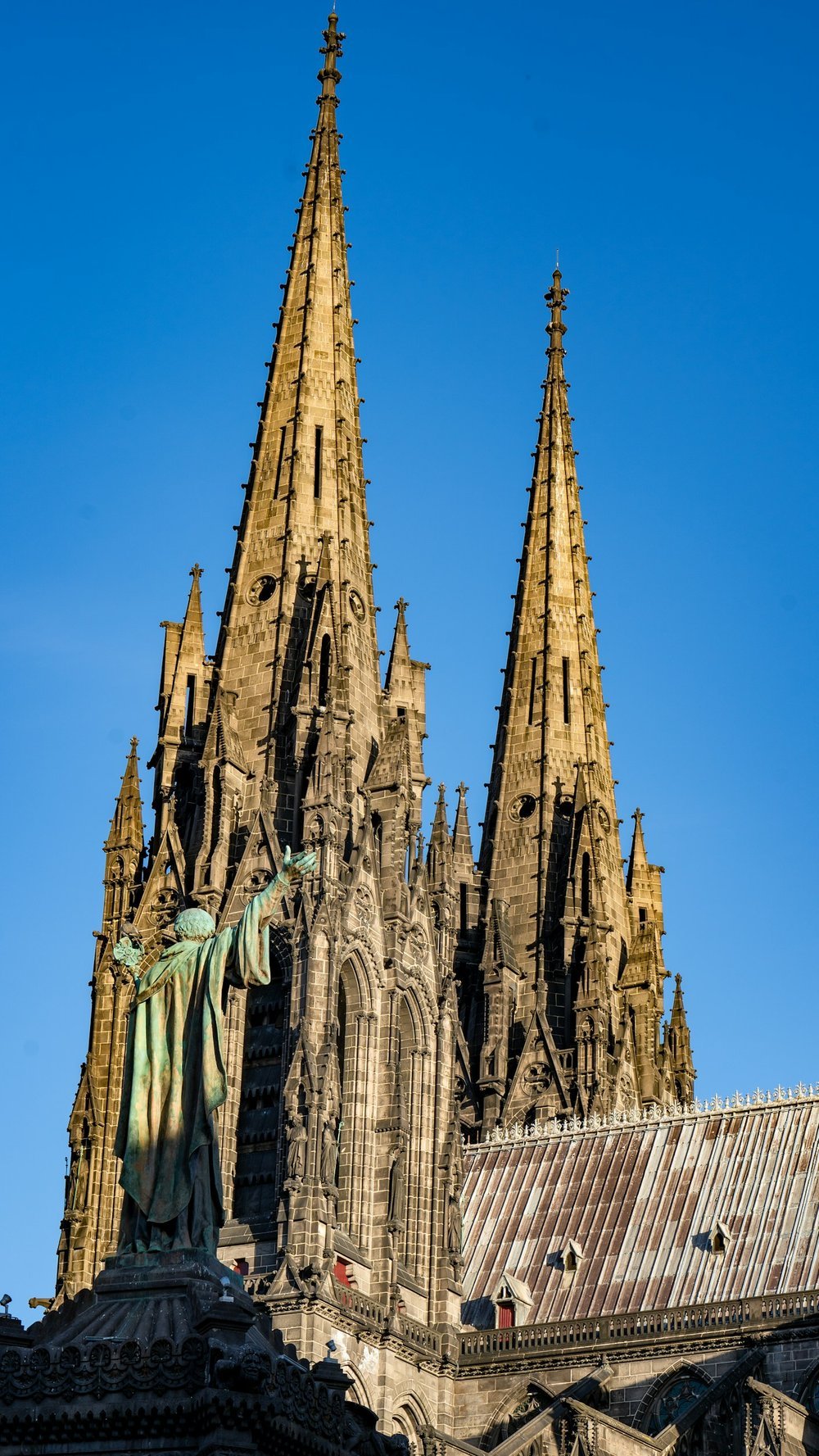 Vue majestueuse des tours gothiques de la cathédrale Notre-Dame à Clermont-Ferrand, avec un ciel bleu en arrière-plan. Idéal pour découvrir notre agence et ses services d’essayage dans cette ville riche en architecture historique.