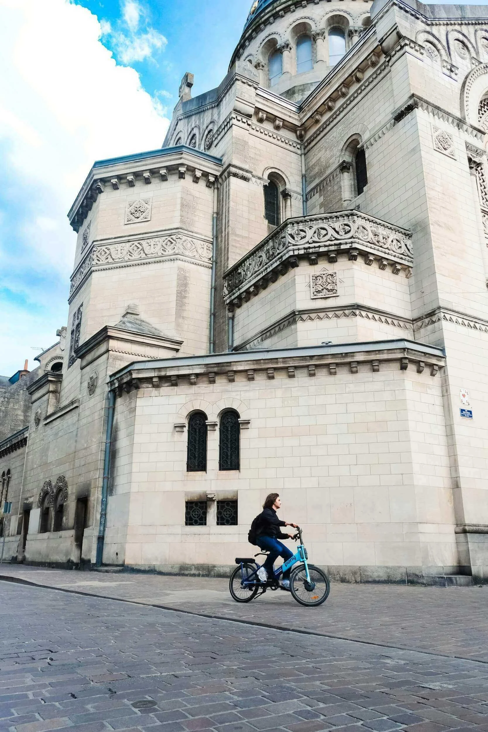Vue d’un bâtiment historique à Tours, avec un cycliste passant devant, reflétant l’architecture élégante et les rues animées de la ville. Idéal pour découvrir notre agence et ses services d’essayage dans cette destination culturelle et dynamique.