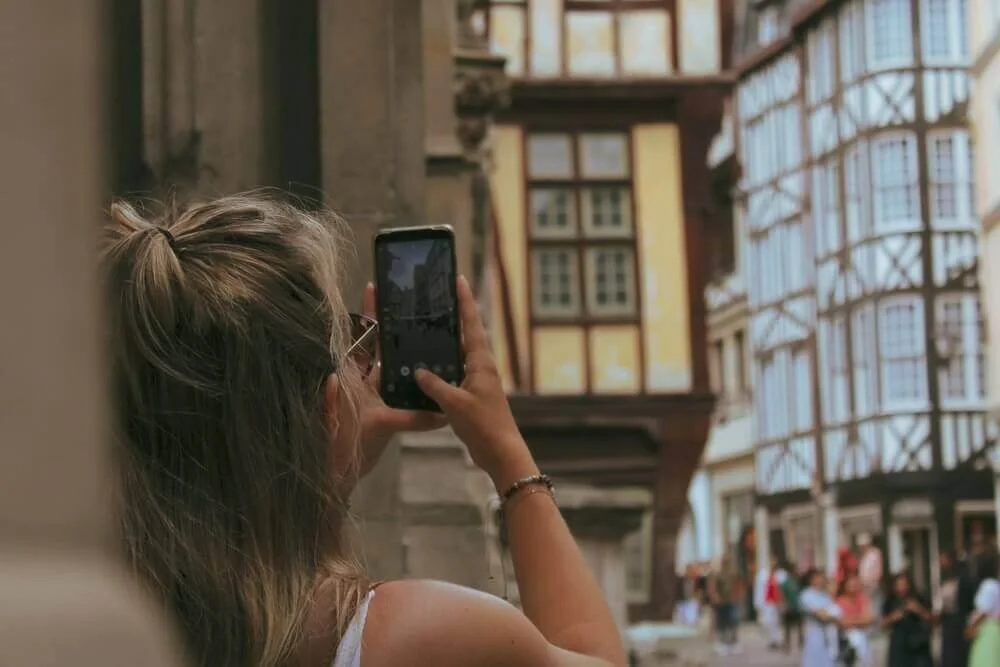 Vue d’une rue piétonne animée à Rouen, avec une femme prenant une photo d’un bâtiment historique. Idéal pour découvrir comment devenir mannequin d’essayage à Rouen, une ville riche en architecture et culture.