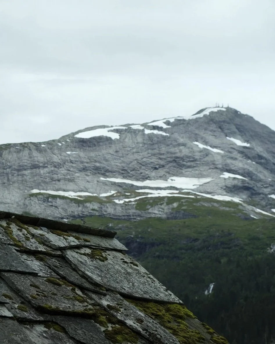 Fjell med snøflekker, sett fra et grått tak med moseflekker.