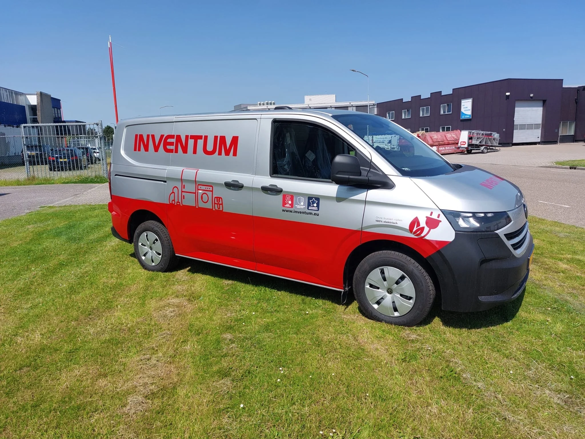 Een gele postkoerier met groene en witte logo's en tekst, geparkeerd op gras onder een blauwe hemel.