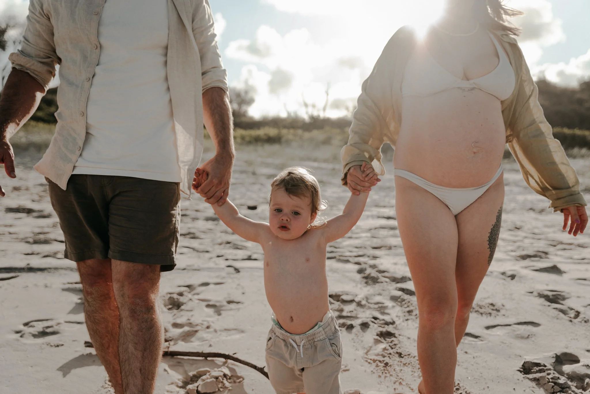 A young child holding hands with two adults, walking on the beach during sunset.