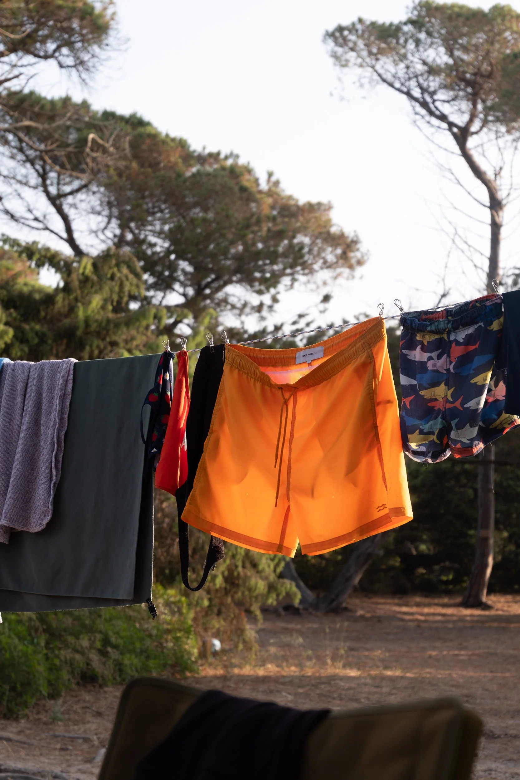 Bunte Kleidung hängt an einer Wäscheleine im Freien, im Hintergrund Bäume und ein Himmel.