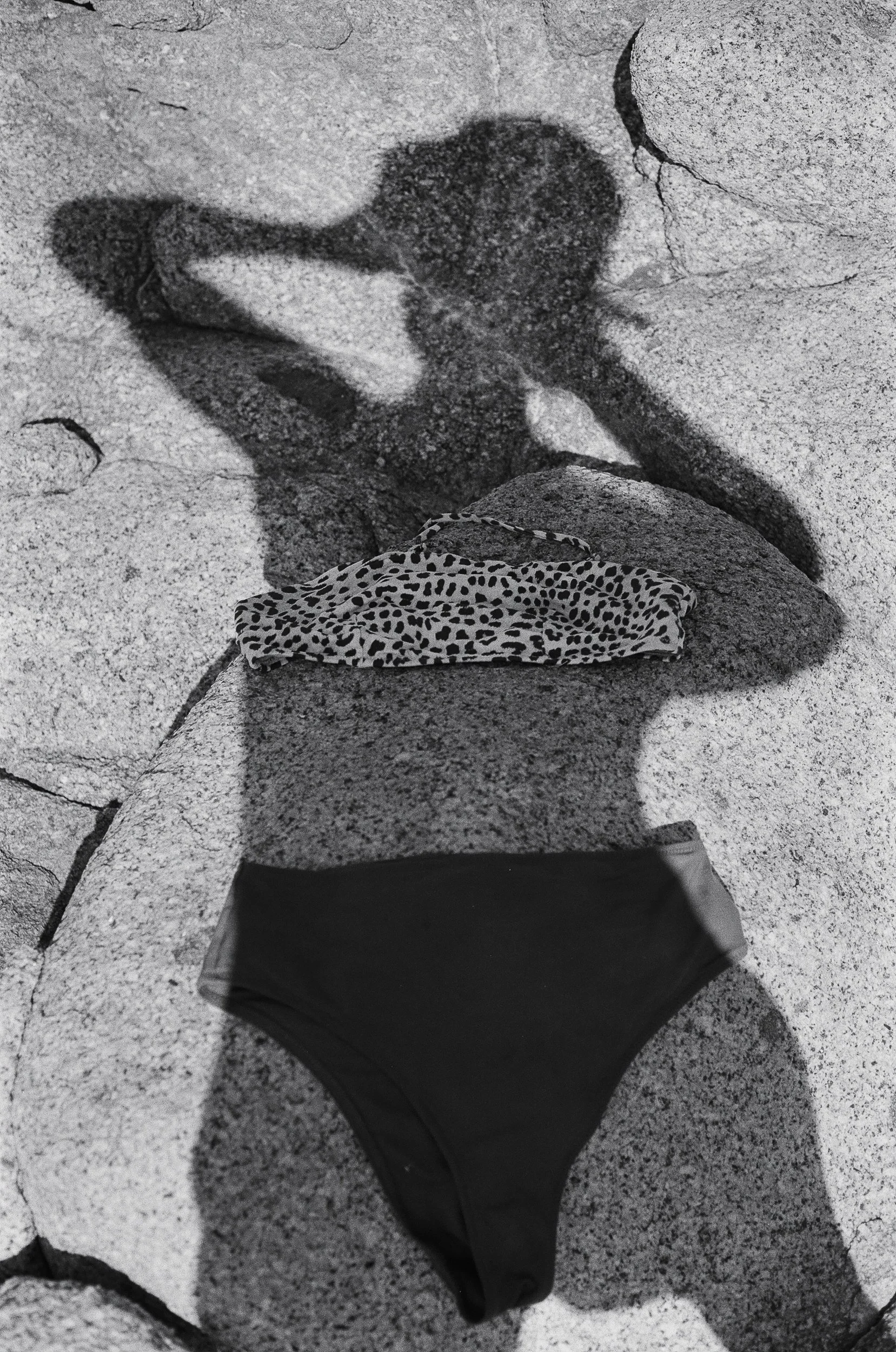 Schatten einer Frau, die Fotografie auf einer felsigen Oberfläche macht, mit einem Leopard-Print Kleid und dunklen Shorts.