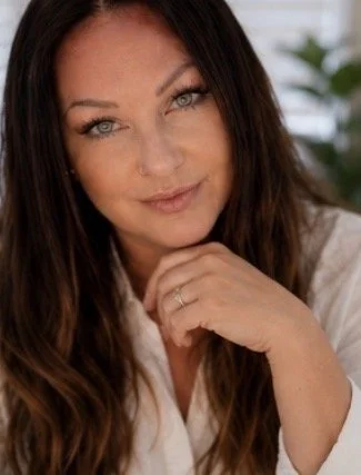 Close-up of Teresa Harris Boag with long brown hair, blue eyes, and fair skin, smiling softly and resting her chin on her hand.