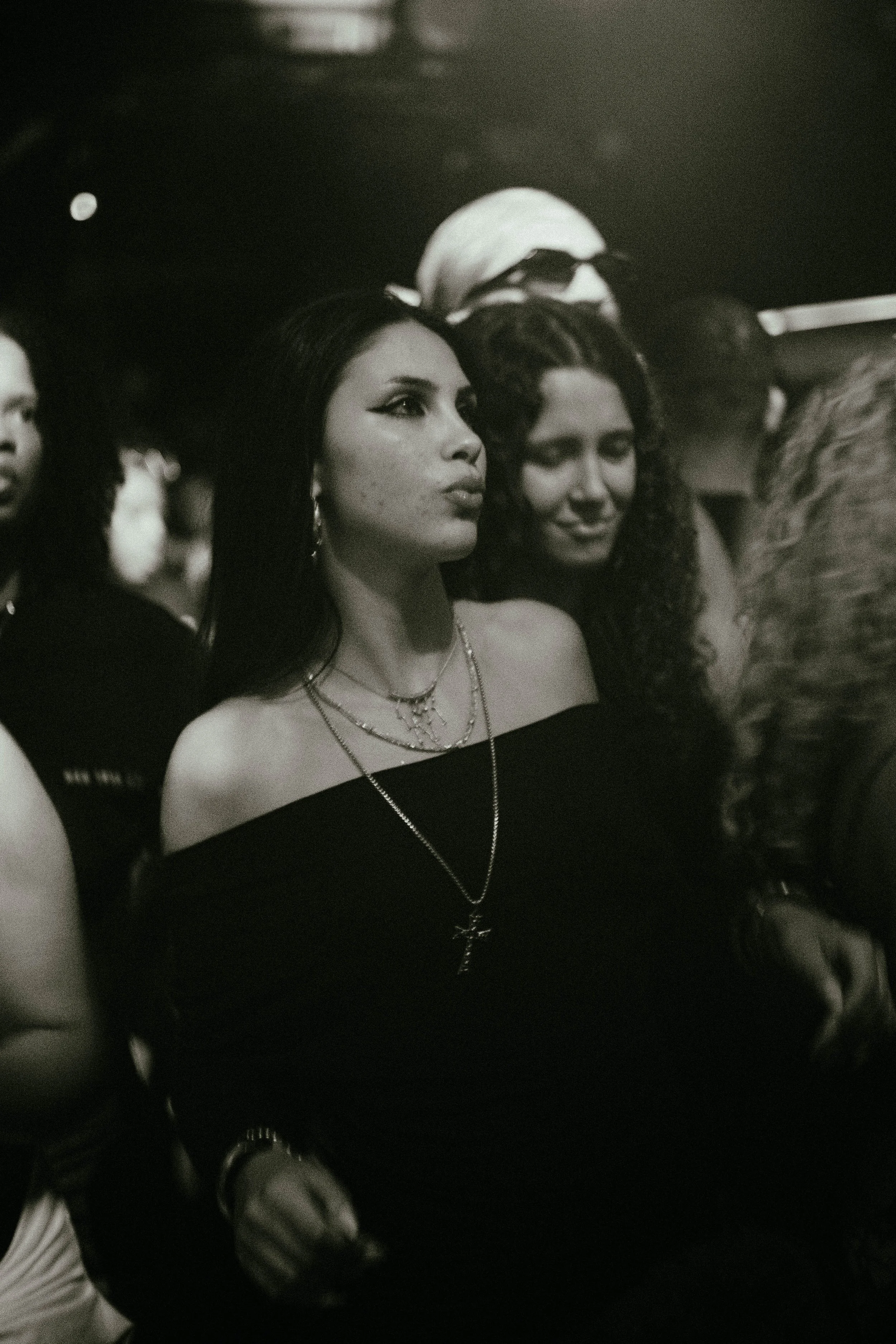 Black and white image of women at a social event, some wearing jewelry, with a woman in the foreground looking attentively.