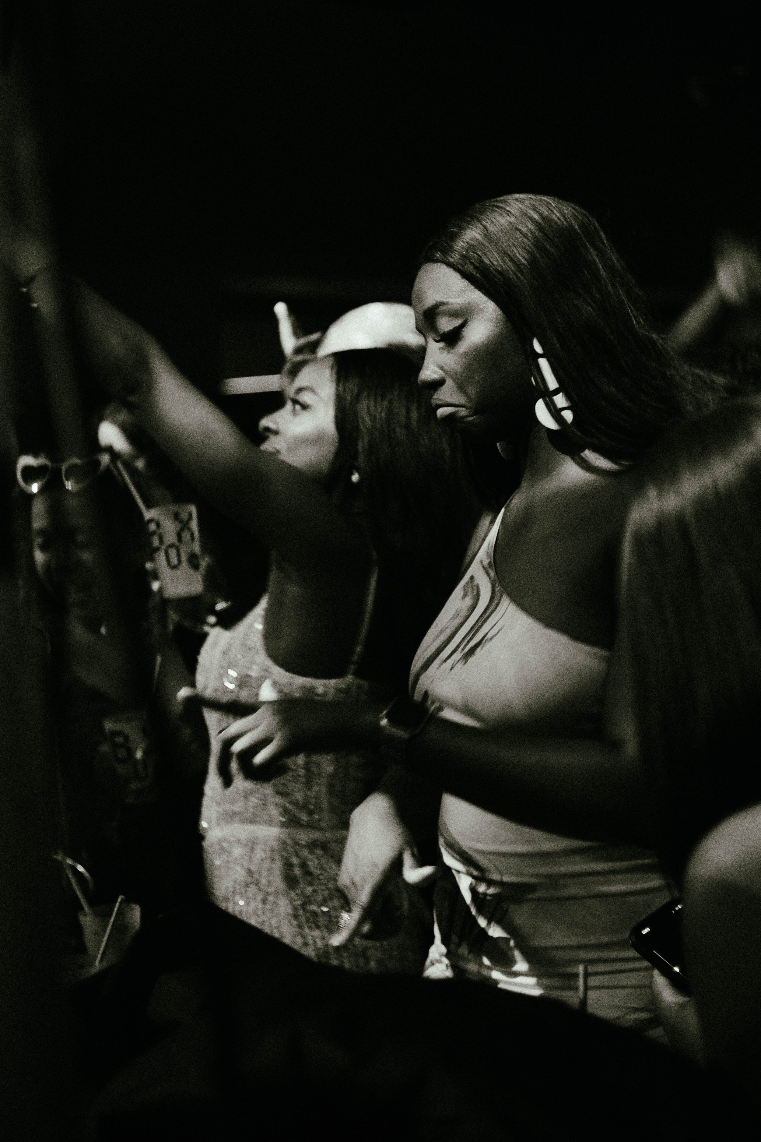 Black and white photo of two women in a crowded setting, one with her eyes closed, the other with her arm stretched out.