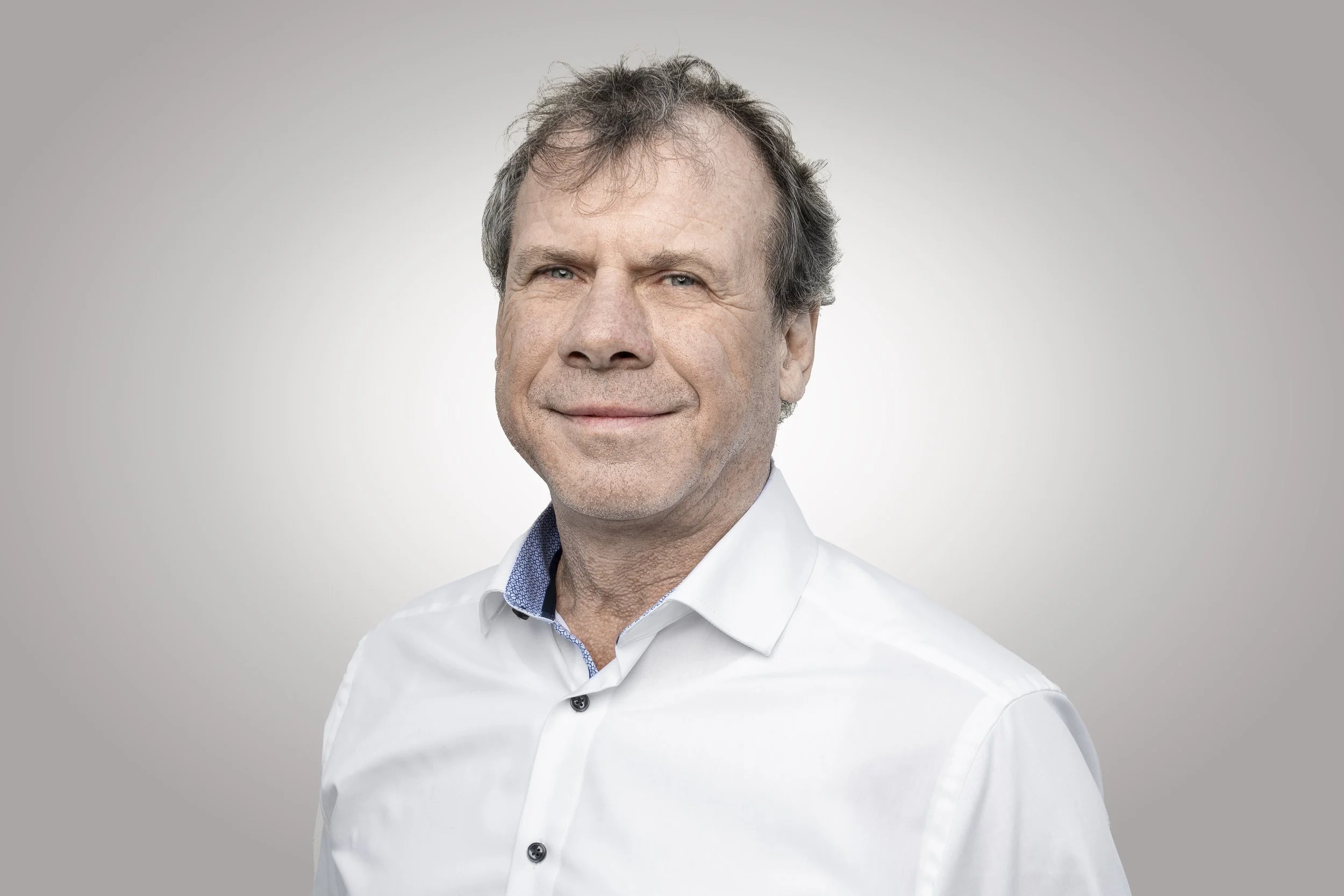 Porträt eines lächelnden Mannes mit Brille und dunklen Haaren, trägt ein weißes Hemd.