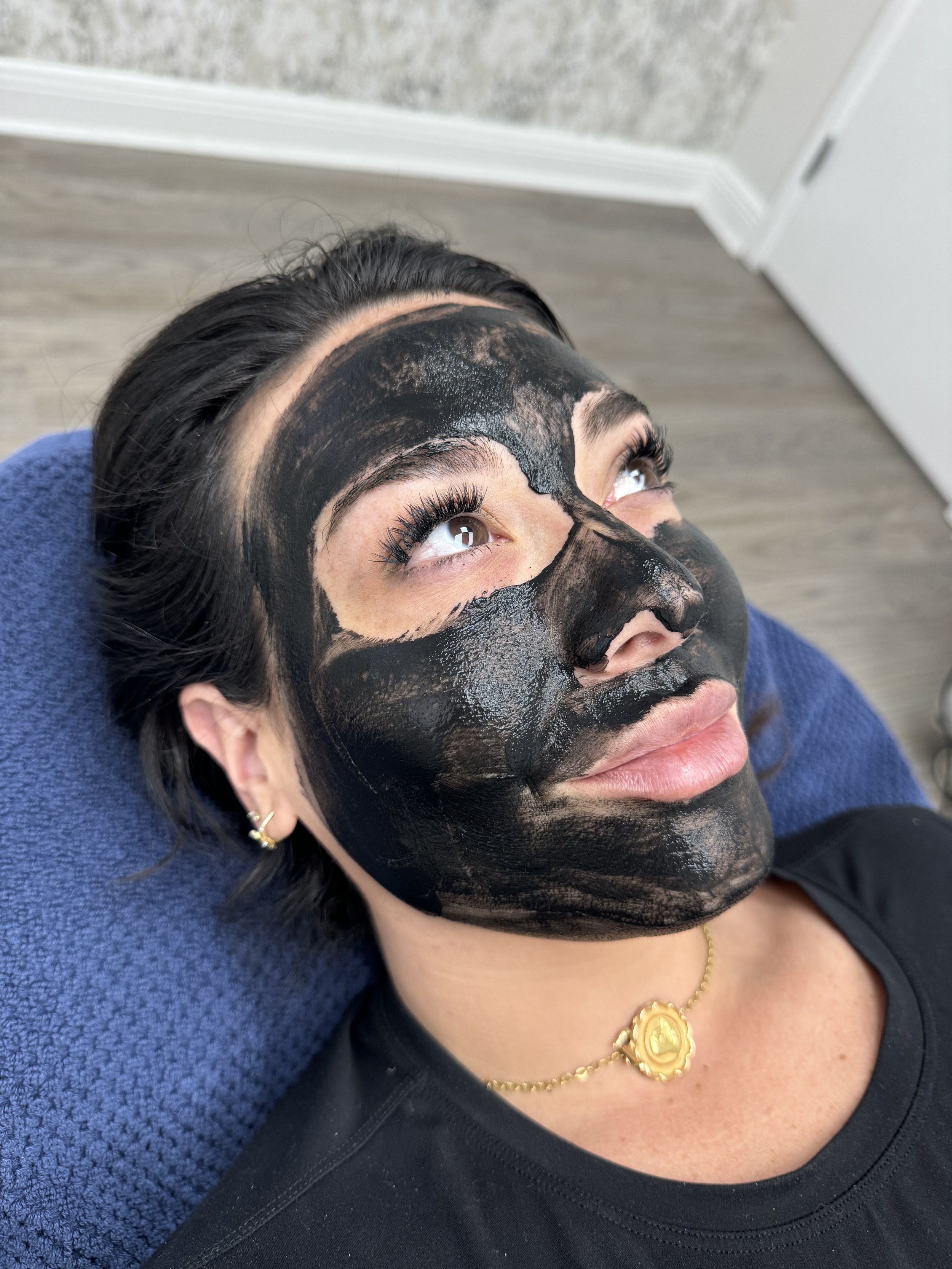 Person relaxing with a black facial mask on their face, lying on a blue towel.