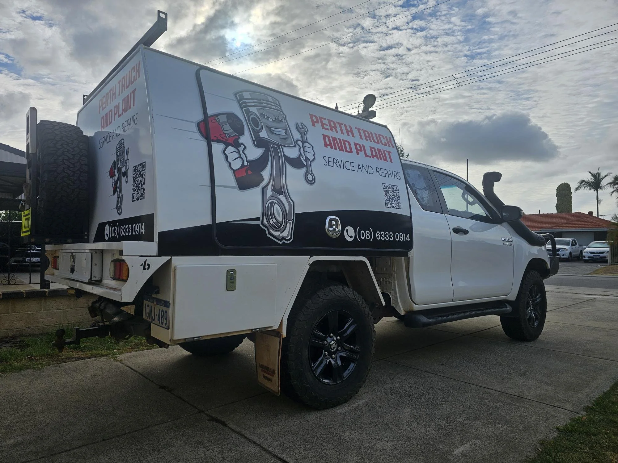 A service truck with advertising for Perth Truch and Plant repair services, including a cartoon engine character holding a wrench, a QR code, phone number, and logo on the side of the vehicle.