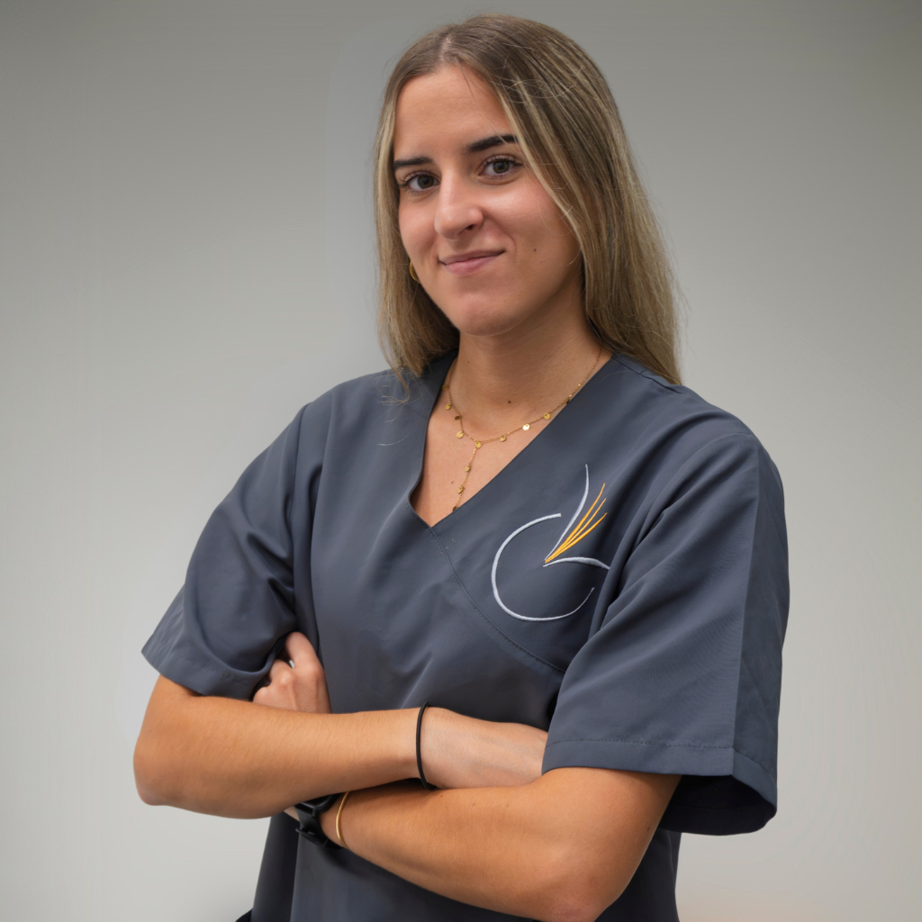 Mujer joven con uniforme gris, brazos cruzados, posando en interior. Se ve confiada y profesional.