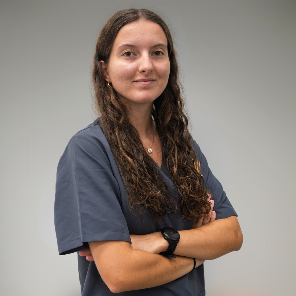 Mujer con uniforme gris en una pose de confianza, en un fondo gris neutro.