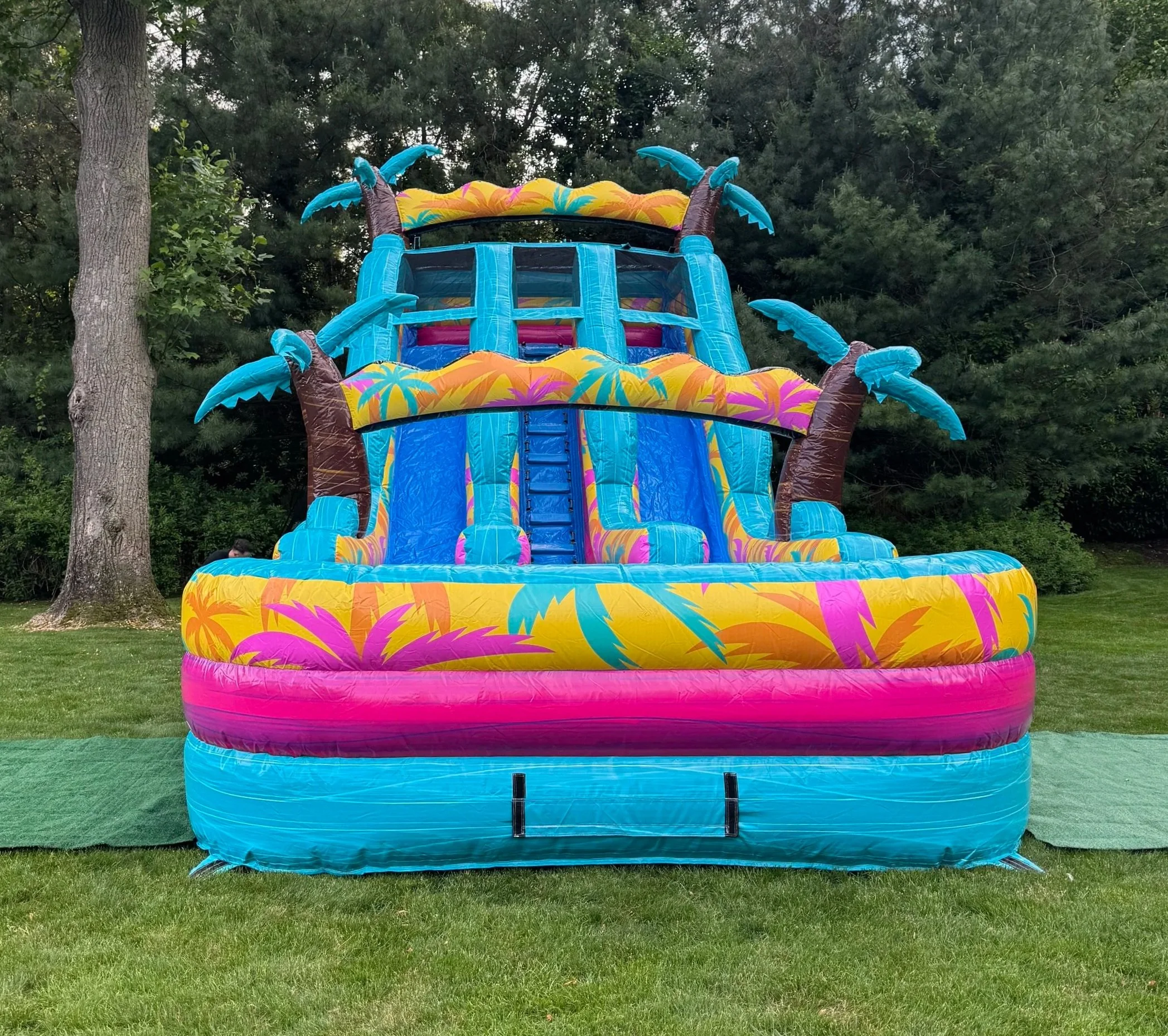 Island sound inflatable water slide rental with tropical palm tree and beach patterns, set up outdoors.