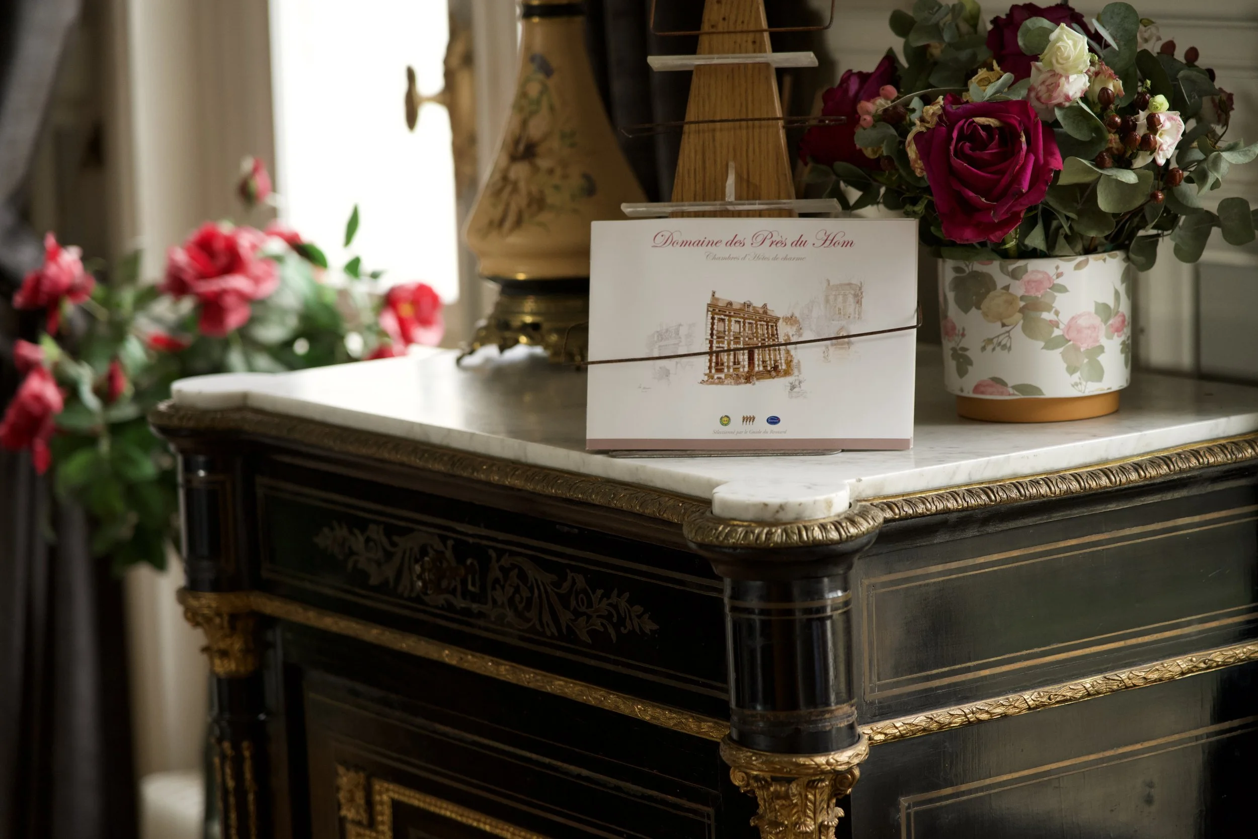 Carte posée sur une commode décorative avec bouquet de fleurs et objet d'art.