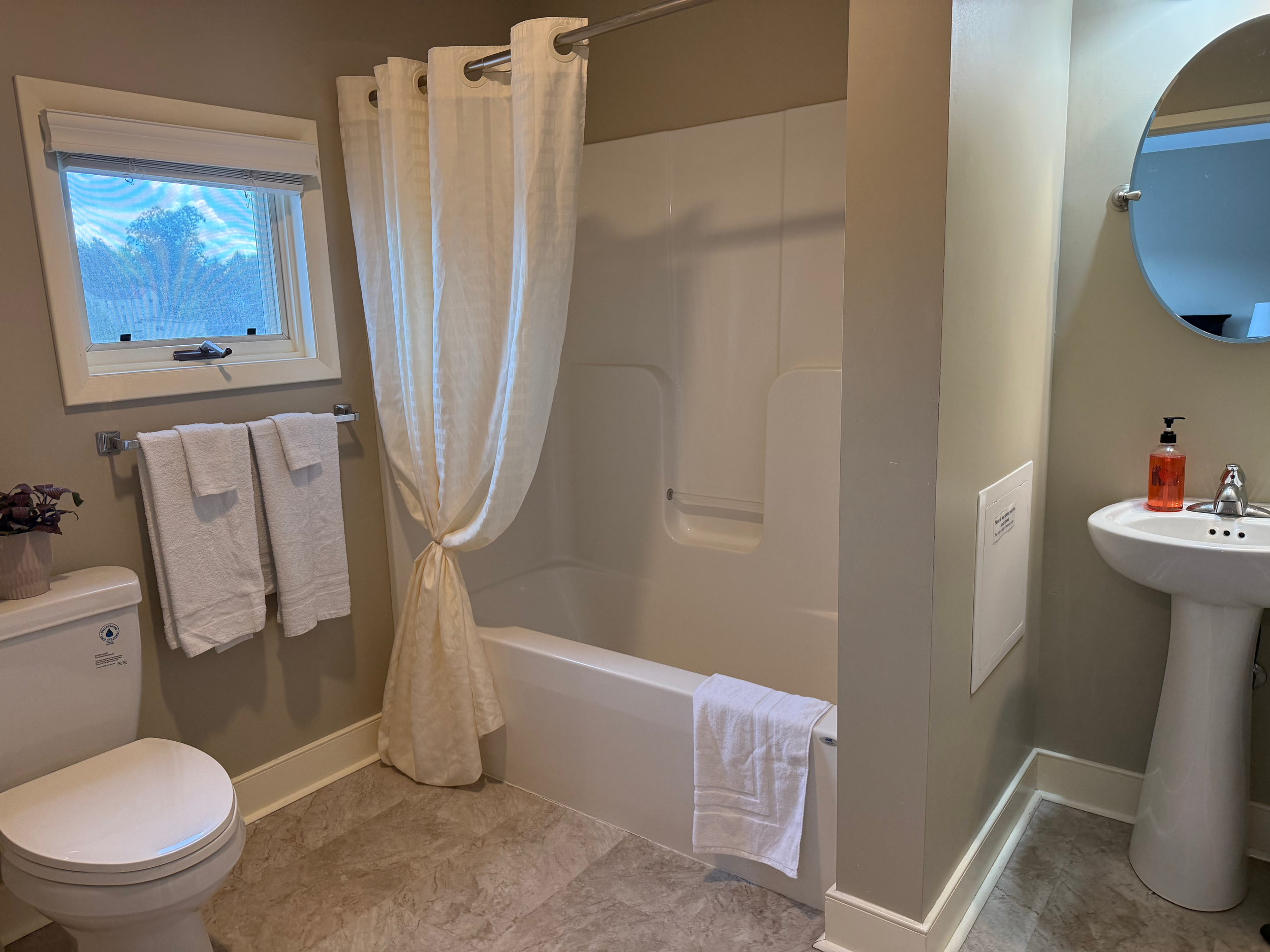 Modern bathroom with bathtub, shower curtain, toilet, pedestal sink, and mirror.