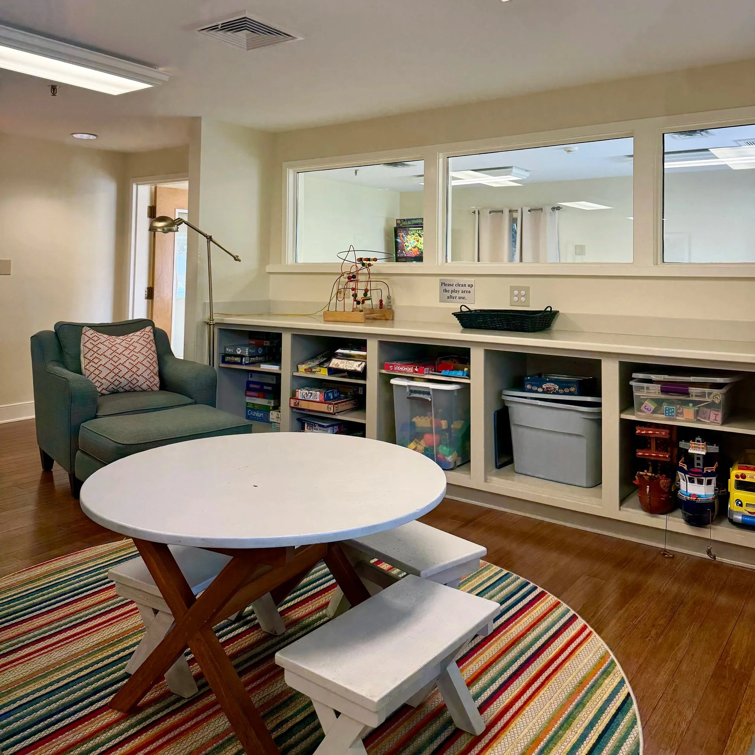 Children's playroom with colorful rug, open shelves, books, toys, and a miniature dollhouse.