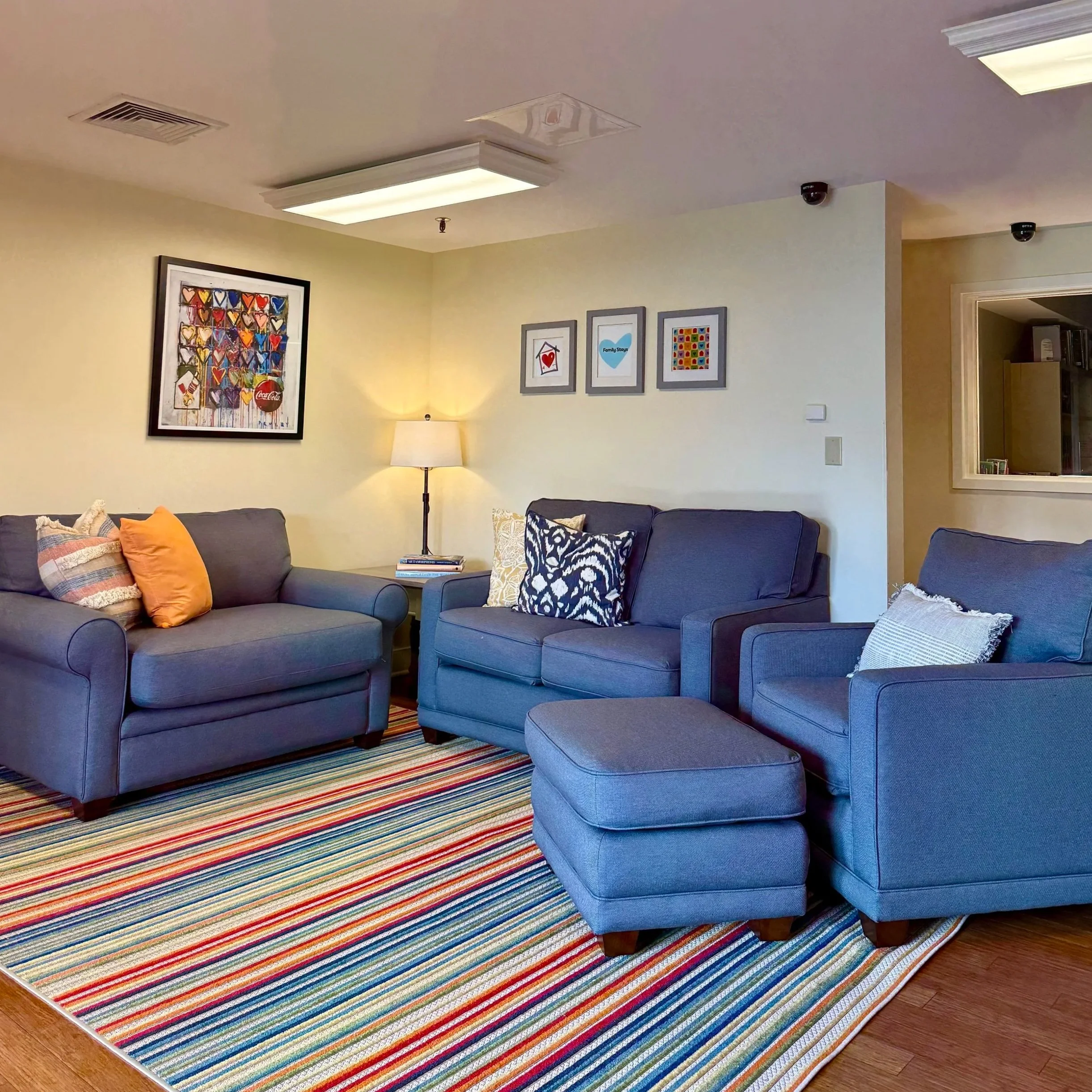 A modern lounge area with comfortable lounge chairs. The room is well-lit with ceiling lights, has wooden flooring, and features a Smart TV. .