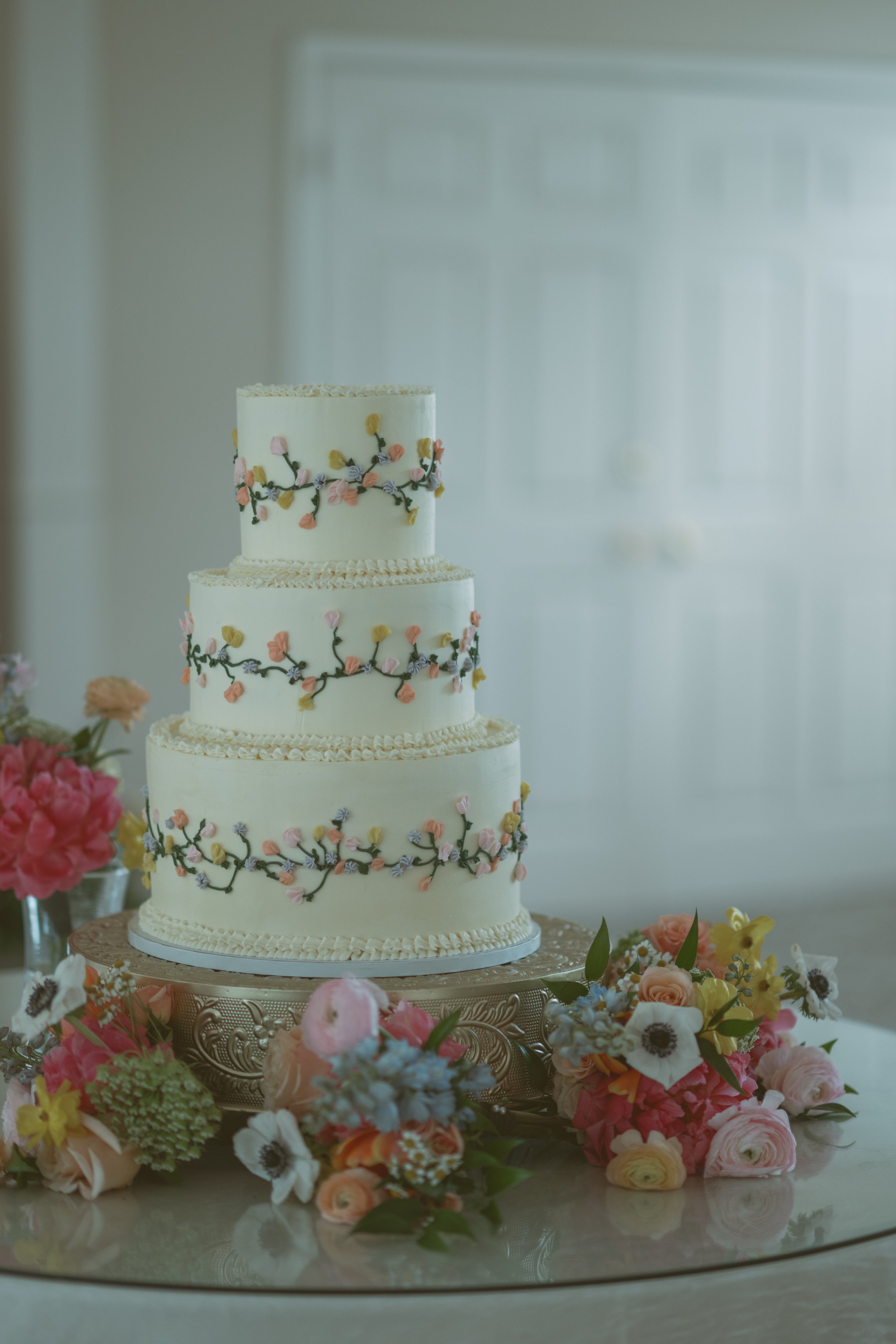 Three tiered cake with floral details and bouquets on the table surrounding it