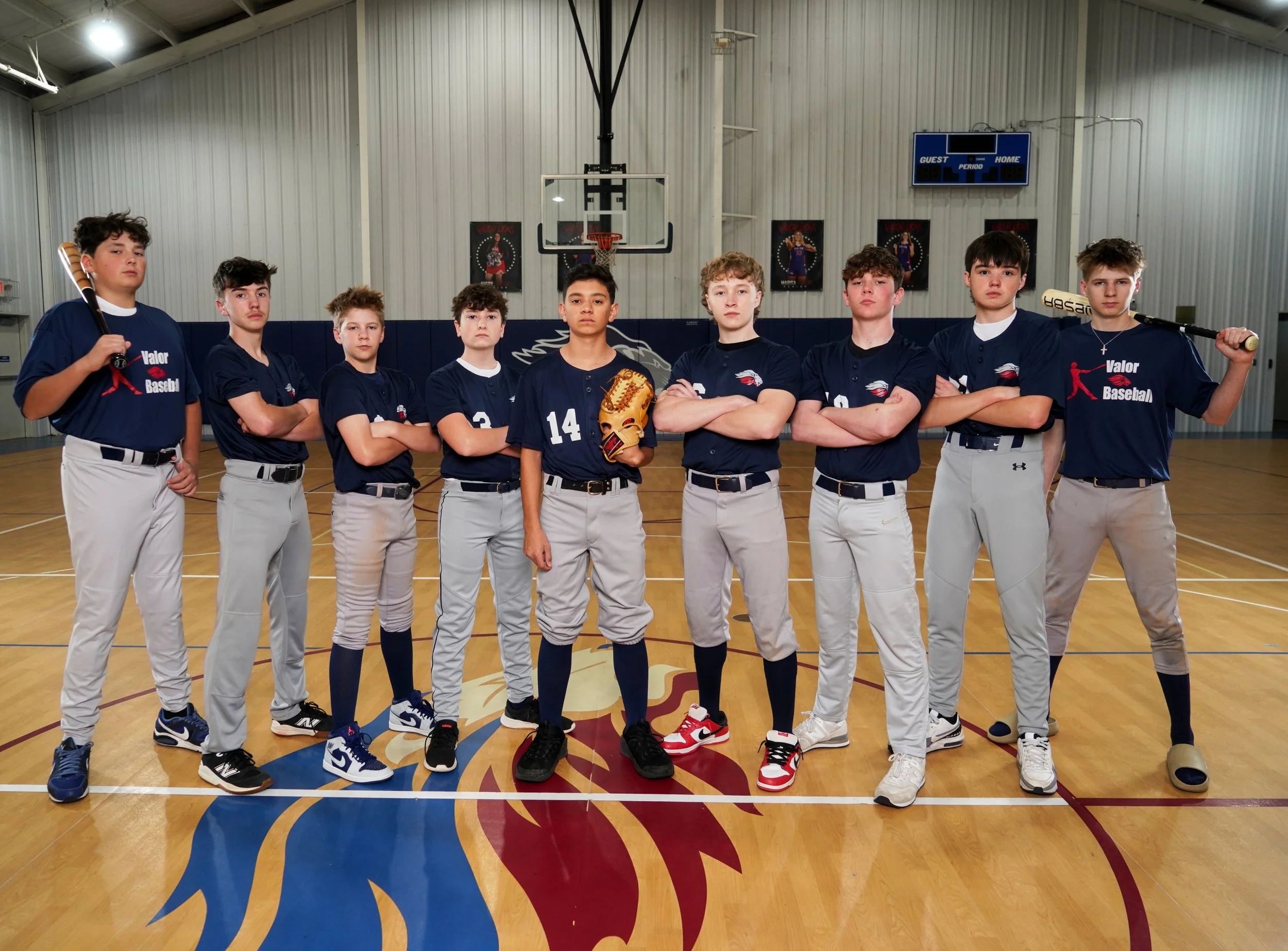 A youth baseball team in uniform poses for a team photo in an indoor gymnasium.