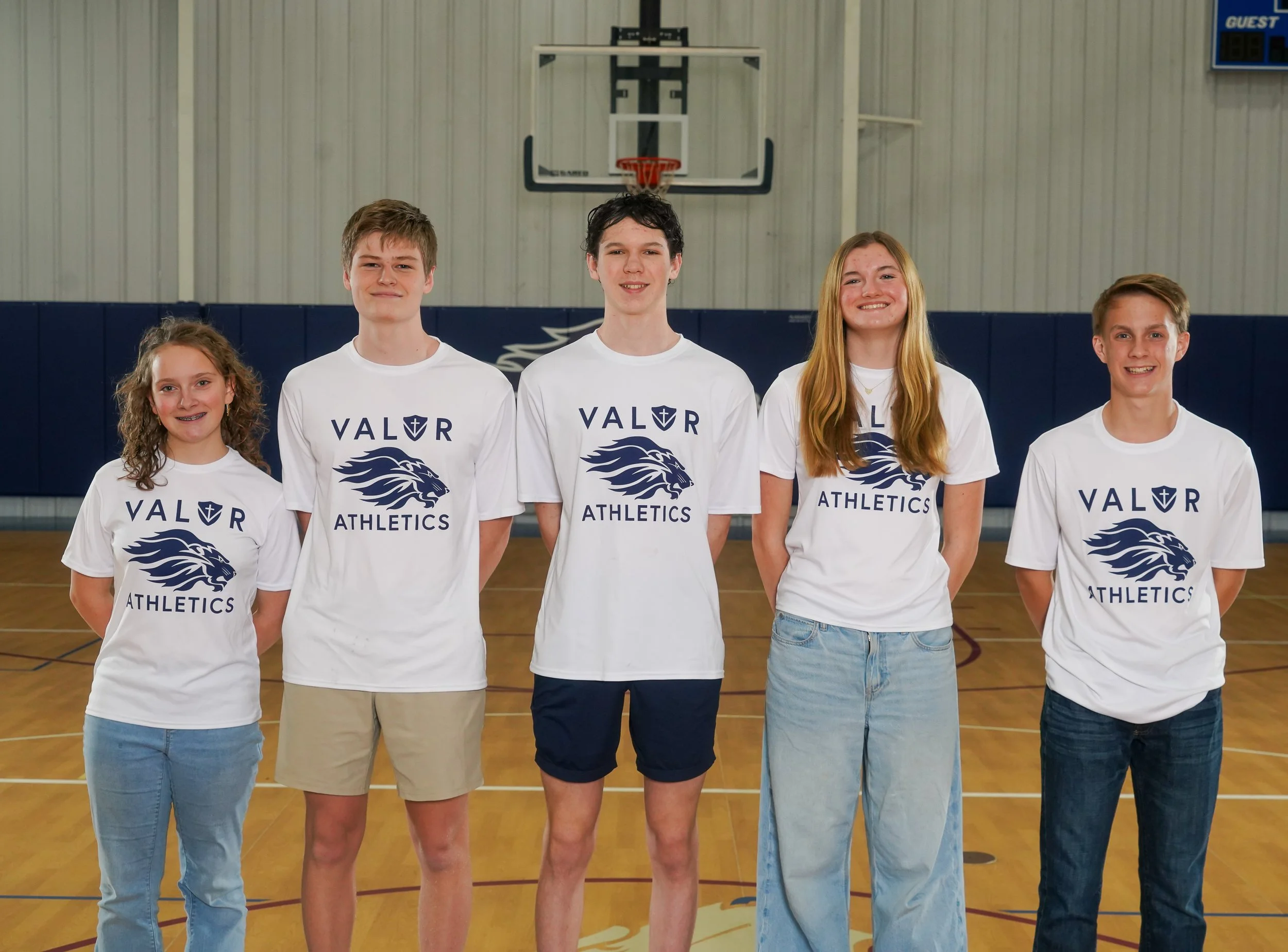 Group of young athletes posing for a photo in an indoor basketball court, wearing red VALOR Athletics shirts.