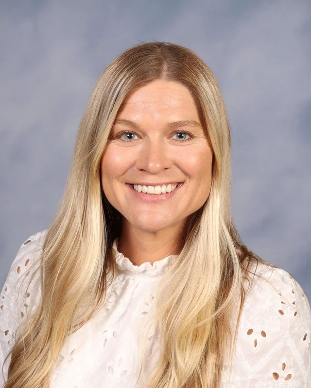 Smiling woman with long blonde hair wearing a white shirt outdoors in a park or garden